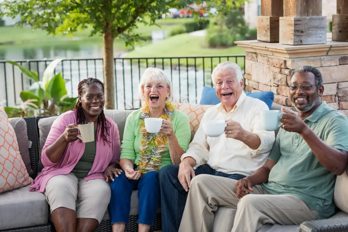 Four older adults laughing together with cups of coffee on an outdoor patio