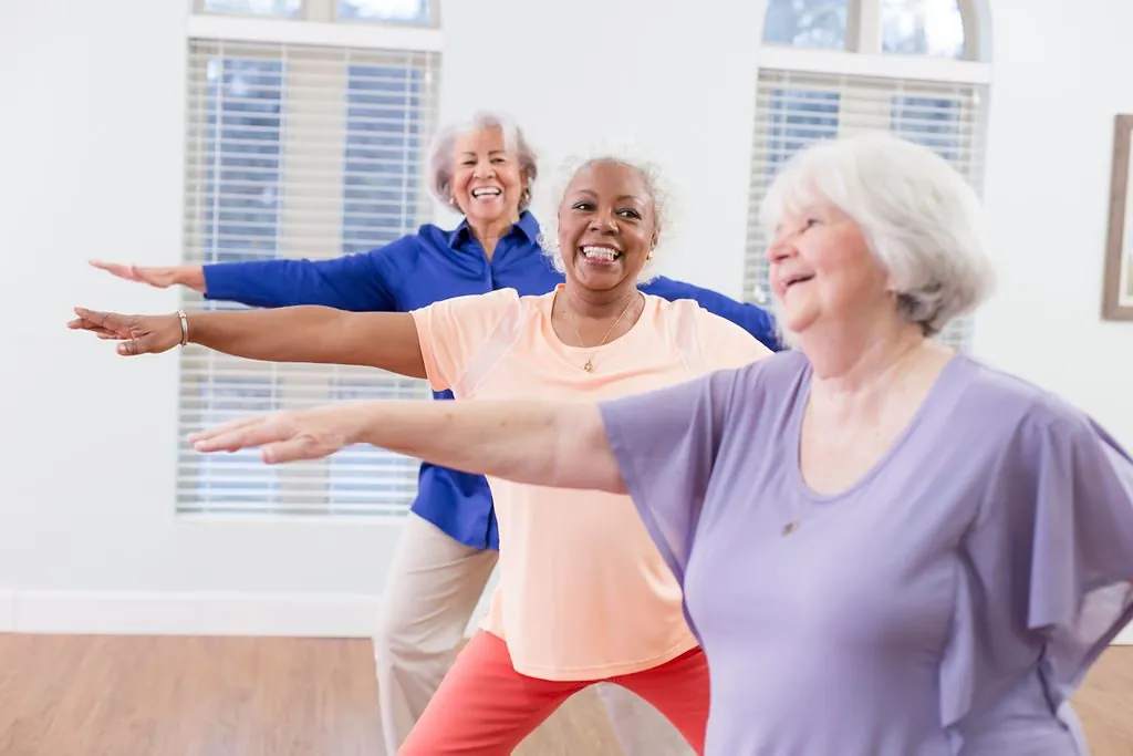 Three older women smiling during a stretching class in a bright room